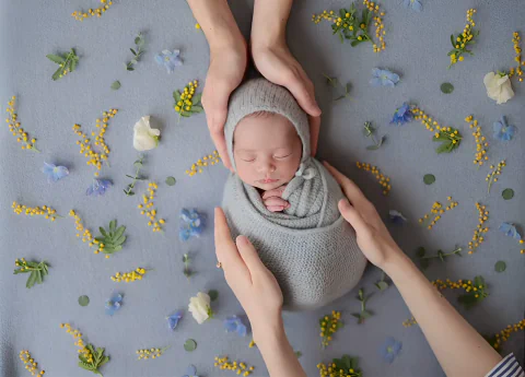 青と黄色の花に囲まれ家族の手に見守られる新生児