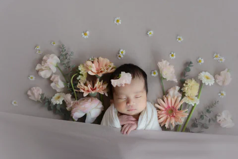 淡いピンクとクリーム色の花に包まれて眠る新生児