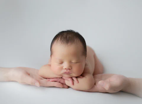 ご家族の重ねた手に頬を添えて眠る新生児