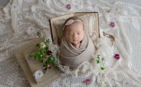 古書と白や紫の小花に囲まれて眠る新生児