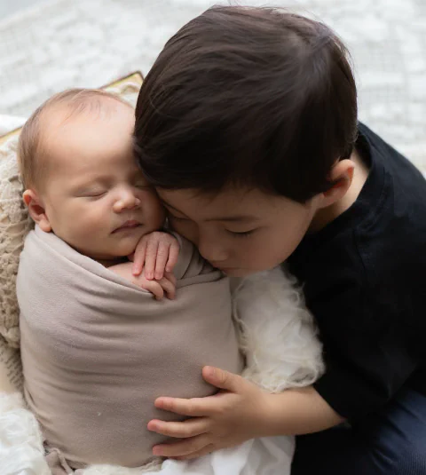 おくるみに包まれた赤ちゃんへきょうだいがキスをする姿