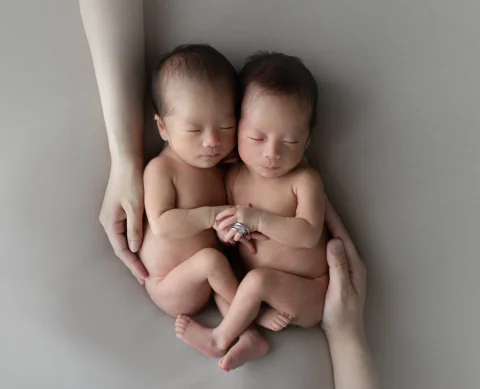 家族の腕に包まれ手を重ねて眠る双子の新生児